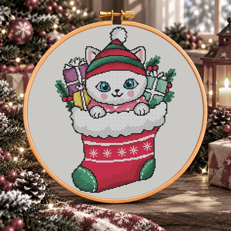 May include: A cross-stitch embroidery in a round wooden hoop featuring a white cat wearing a red and green striped hat, peeking out of a red and white Christmas stocking filled with colorful wrapped gift boxes and green holly sprigs.