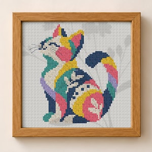 May include: A cross-stitch embroidery of a cat in a wooden frame. The cat is composed of geometric color blocks in navy blue, bright yellow, pink, teal, and white, featuring stylized leaf patterns on its body and a curved, multi-colored tail.