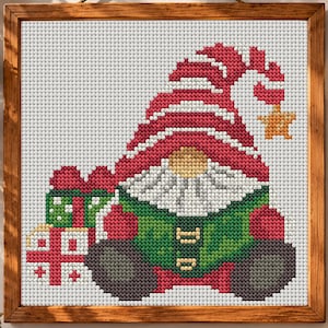 May include: A cross-stitch pattern in a wooden frame featuring a gnome wearing a large red hat with a yellow star at the tip. The gnome has a white beard, a green tunic, and dark gray boots, and is positioned next to two wrapped gift boxes.