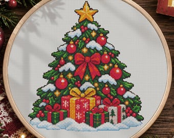 May include: A cross-stitch pattern in a wooden embroidery hoop featuring a green Christmas tree decorated with red ornaments, a large red bow, and a yellow star topper, surrounded by wrapped gift boxes on a snowy base.