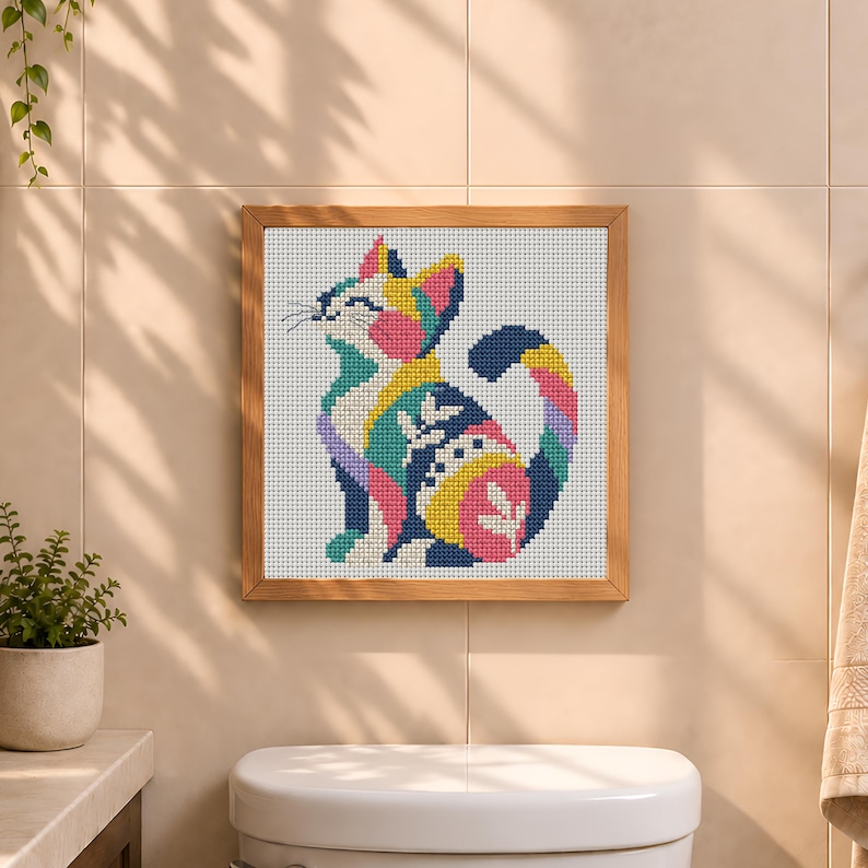 May include: A square cross-stitch embroidery featuring a stylized cat in a seated position. The cat is composed of vibrant, multi-colored geometric patterns including pink, yellow, blue, and green, all set against a white grid fabric in a wooden frame.