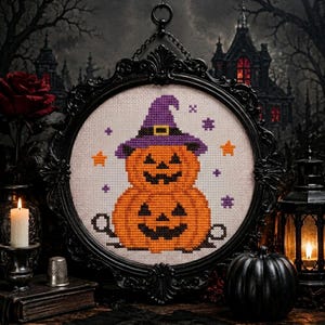 May include: A cross-stitch embroidery featuring a stacked pumpkin character wearing a purple witch hat with a yellow buckle, surrounded by small orange stars and purple crosses, encased in an ornate black oval frame with a hanging chain.