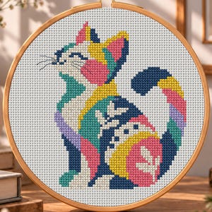 May include: A cross-stitch embroidery project featuring a stylized cat in a circular wooden hoop. The cat design uses a vibrant color palette of navy blue, yellow, pink, teal, and lavender, with white leaf-like patterns on its body.