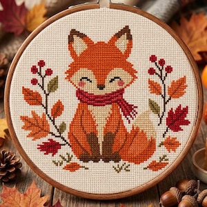 May include: A circular wooden embroidery hoop containing a cross-stitch pattern of a fox with orange fur, brown paws, and a red scarf. The fox is surrounded by autumn-themed elements including red berries and maple leaves in shades of red and orange.