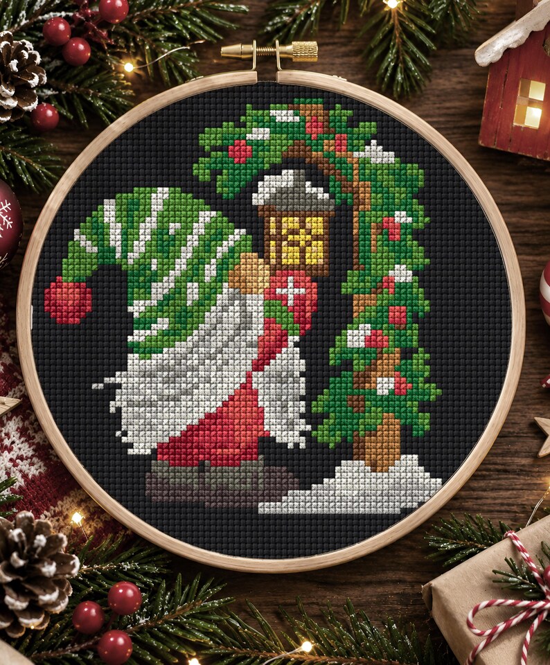 May include: A circular wooden embroidery hoop containing a cross-stitch pattern on black fabric. The design features a gnome wearing a green and white striped hat, a long white beard, and red clothing, standing beside a green Christmas tree.