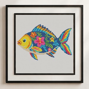 Pode incluir: Um bordado em ponto cruz de um peixe numa moldura preta. O peixe tem uma cabe&ccedil;a amarela e um corpo azul escuro com um padr&atilde;o de flores de hibisco cor-de-rosa, folhas verdes e detalhes amarelos. As barbatanas e a cauda apresentam riscas vibrantes.