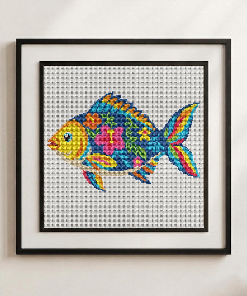 Pode incluir: Um bordado em ponto cruz de um peixe numa moldura preta. O peixe tem uma cabe&ccedil;a amarela e um corpo azul escuro com um padr&atilde;o de flores de hibisco cor-de-rosa, folhas verdes e detalhes amarelos. As barbatanas e a cauda apresentam riscas vibrantes.