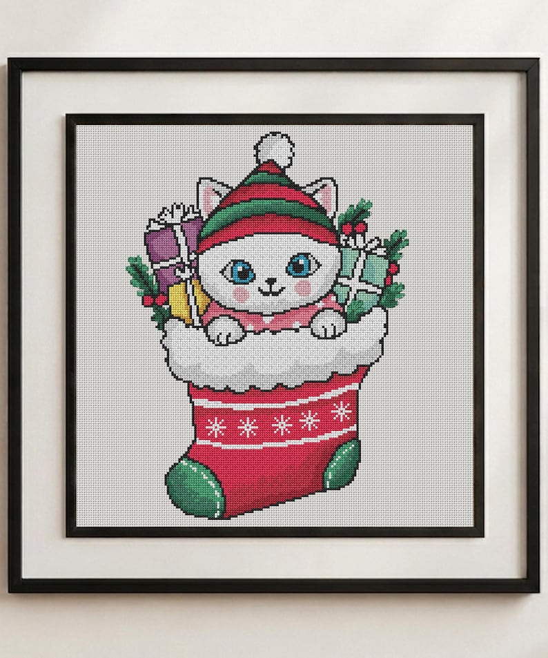 May include: A cross-stitch pattern featuring a white cat with blue eyes wearing a red and green striped hat, sitting inside a red Christmas stocking. The cat is surrounded by wrapped gift boxes, holly leaves, and berries.