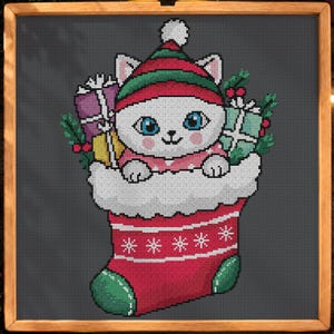 May include: A cross-stitch pattern on a dark gray background featuring a white cat with blue eyes wearing a red and green hat, tucked inside a red Christmas stocking with white trim, surrounded by wrapped gifts and holly sprigs.