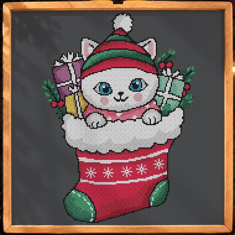 May include: A cross-stitch pattern on a dark gray background featuring a white cat with blue eyes wearing a red and green hat, tucked inside a red Christmas stocking with white trim, surrounded by wrapped gifts and holly sprigs.