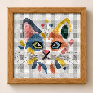 K&ouml;nnte beinhalten: Eine Kreuzstichstickerei eines Katzengesichts in einem hellen Holzrahmen. Die Katze hat eine wei&szlig;e Grundfarbe mit blauen, orangefarbenen, gelben und rosafarbenen Flecken. Sie hat gr&uuml;ne und blaue Augen, eine rosa Nase und schwarze Schnurrhaare.