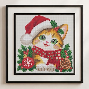 May include: A framed cross-stitch embroidery featuring a ginger and white kitten wearing a red Santa hat and a red scarf with white patterns. The kitten is surrounded by green holly leaves, red berries, a red Christmas ornament, and a pinecone.