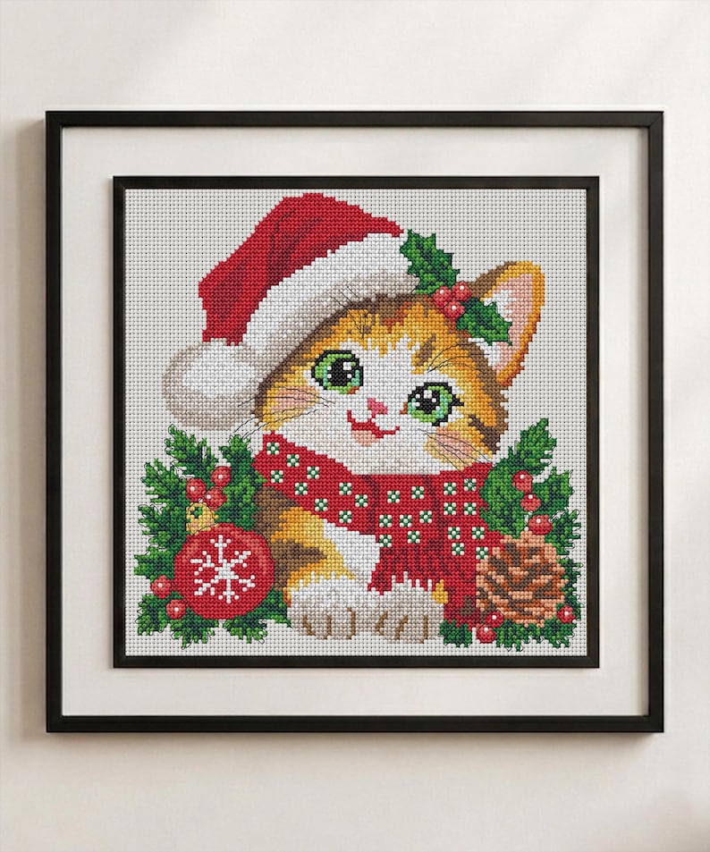 May include: A framed cross-stitch embroidery featuring a ginger and white kitten wearing a red Santa hat and a red scarf with white patterns. The kitten is surrounded by green holly leaves, red berries, a red Christmas ornament, and a pinecone.