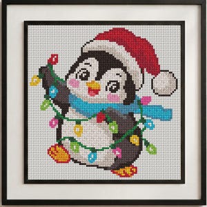 May include: A framed cross-stitch embroidery featuring a penguin wearing a red Santa hat and a blue scarf. The penguin is wrapped in a string of colorful Christmas lights with yellow, pink, blue, and green bulbs against a white grid background.