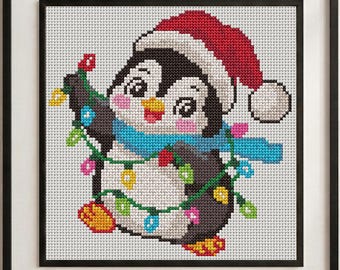 May include: A framed cross-stitch embroidery featuring a penguin wearing a red Santa hat and a blue scarf. The penguin is wrapped in a string of colorful Christmas lights with yellow, pink, blue, and green bulbs against a white grid background.