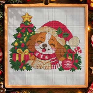 May include: A cross-stitch pattern featuring a brown and white puppy wearing a red Santa hat and a matching scarf. The puppy is positioned next to a decorated Christmas tree, a red gift box with a yellow bow, and a red ornament with a white snowflake.