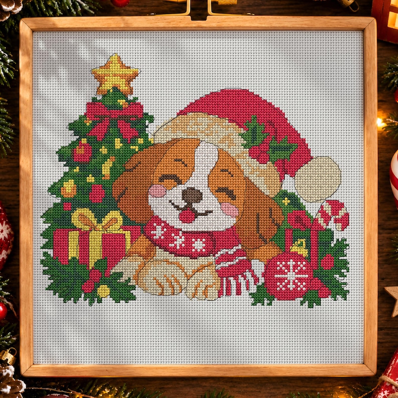 May include: A cross-stitch pattern featuring a brown and white puppy wearing a red Santa hat and a matching scarf. The puppy is positioned next to a decorated Christmas tree, a red gift box with a yellow bow, and a red ornament with a white snowflake.