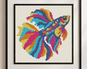 May include: A framed cross-stitch embroidery featuring a vibrant betta fish with flowing fins in shades of bright pink, electric blue, and sunny yellow against a white grid fabric background, enclosed within a simple black square frame.