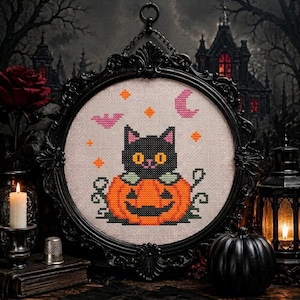 May include: A cross-stitch embroidery featuring a black cat sitting inside an orange jack-o'-lantern, surrounded by a pink crescent moon, a pink bat, and orange stars, displayed in an ornate black oval frame with a hanging chain.