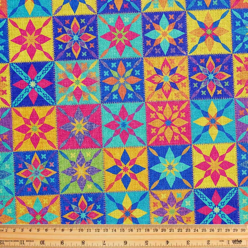 Op de afbeelding: Een stof met een herhalend rasterpatroon van veelkleurige achtpuntige sterren in tinten roze, geel, blauw en groen. Een houten liniaal is onderaan geplaatst en toont afmetingen in inches van 0 tot 30.