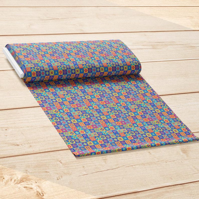 Op de afbeelding: Een rol stof met een herhalend geometrisch patroon van kleine vierkantjes in levendige tinten blauw, oranje, geel, groen en paars. Het textiel is aan &eacute;&eacute;n kant gevouwen en toont een dicht, kleurrijk raster van gedetailleerde stervormige motieven.