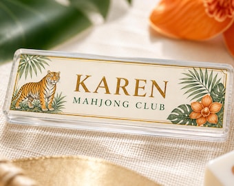 May include: A rectangular clear acrylic name plate featuring the text KAREN and MAHJONG CLUB in gold and dark green lettering. The design includes a tiger illustration on the left and tropical palm leaves with an orange flower on the right.