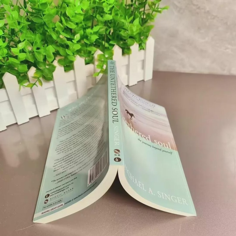 May include: An open book titled "The Untethered Soul" by Michael A. Singer. The cover features a gradient of blue and white with a silhouette of a horse. The spine reads "THE UNTETHERED SOUL SINGER".