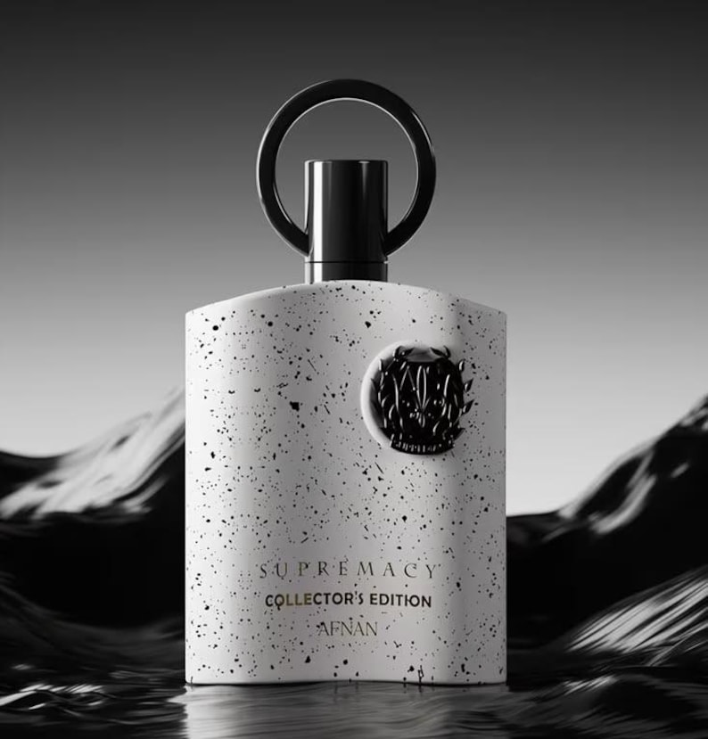 Puede incluir: Un frasco de perfume blanco y negro moteado con un asa de anillo negro. El frasco tiene un emblema negro y las palabras "SUPREMACY COLLECTOR'S EDITION AFNAN" impresas en la parte delantera. El fondo es una imagen en escala de grises de olas.