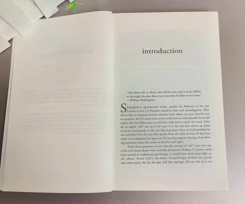 May include: An open book with the word "introduction" at the top of the right page. The text includes a quote by William Shakespeare and a discussion of self-perception and psychology.