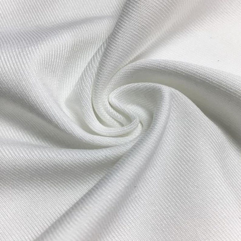 Pode incluir: Um tecido branco s&oacute;lido com uma textura canelada distinta com linhas verticais. O material &eacute; reunido num redemoinho central, criando dobras suaves e fluidas e sombras que destacam o padr&atilde;o consistente e a cor branca brilhante em todo o tecido.
