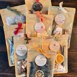 May include: Eight stand-up pouches containing dried botanical potpourri blends, each with a circular label featuring names like Coffee Cake, Fresh & Cozy, Tropical Getaway, Vanilla Chai, Banana Split, Ginger Snap Magic, Coconut Splash, and Clean Breeze.