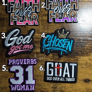 Pode incluir: Seis emblemas bordados com bordas pretas. Os emblemas 1 e 2 dizem Faith over Fear em rosa ou roxo com padrões castanhos. O emblema 3 diz God got me em prata e rosa. O emblema 4 diz Chosen em azul com uma coroa dourada. O emblema 5 diz Proverbs 31 Woman. O emblema 6 diz GOAT God over all things com uma cruz vermelha.