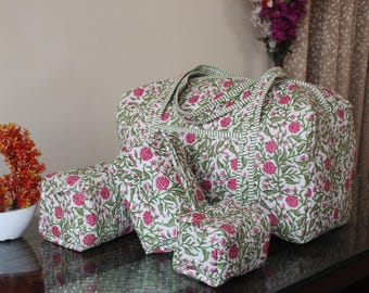 May include: A quilted travel set consisting of a large rectangular duffel bag and three smaller matching pouches of varying sizes. Each piece features a white base with a repeating floral pattern of pink blossoms and green leafy vines throughout.