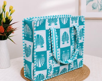 May include: A rectangular tote bag featuring a teal and white checkered pattern with a repeating seashell motif in each square. The bag has two matching fabric handles, a structured boxy shape, and a white zipper closure along the top edge.