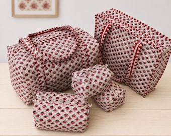 May include: A set of four quilted fabric bags in varying sizes, featuring a repeating pattern of red and black floral motifs on a cream background. Each bag includes a zippered closure and matching fabric handles with red and white striped trim.