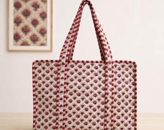 May include: A rectangular quilted tote bag featuring a repeating floral pattern in red and dark blue on a cream background. The bag has two long shoulder straps and edges trimmed with a red and white striped fabric, creating a structured look.