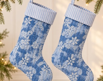 May include: Two quilted Christmas stockings featuring a blue and white floral pattern. Each stocking has a light blue and white striped cuff and a matching hanging loop. The fabric has a vertical quilted texture throughout the body.