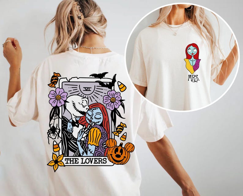 May include: An off-white t-shirt featuring a back graphic of a tarot card titled THE LOVERS with Jack and Sally characters, surrounded by pumpkins, bats, and flowers. The front chest area displays a small graphic of Sally and the text MRS.