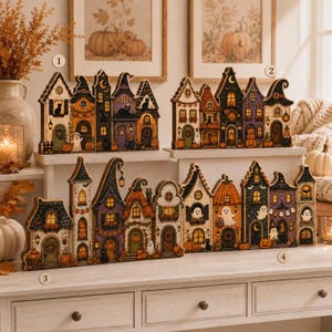 May include: Four illuminated wooden Halloween village displays featuring intricate cutouts of houses, ghosts, black cats, and pumpkins. Each structure is painted in shades of orange, purple, black, and cream, with warm interior lighting visible through windows.