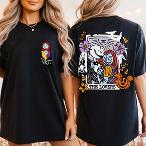 May include: A black t-shirt featuring a small graphic of Sally on the front left chest with the text "Mrs. Watt". The back displays a large tarot card illustration of Jack and Sally titled "THE LOVERS" with bats, flowers, and pumpkins.