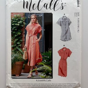 May include: McCall's sewing pattern R10444 for a button-front shirt dress with short sleeves and a belt. The envelope features a photograph of a person wearing the coral-colored striped dress, along with line drawings for views A and B.