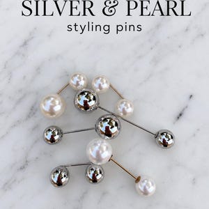 May include: A collection of styling pins featuring a mix of lustrous white pearls and polished silver-tone spheres. The text SILVER & PEARL styling pins is displayed above the pins, which are arranged in a cluster on a white marble surface.