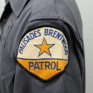 May include: A gray uniform shirt with a black and yellow patch that reads "Palisades Brentwood Patrol" with a blue star in the center.