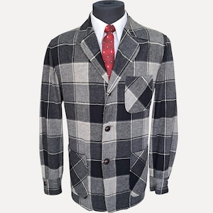 Puede incluir: Un blazer de cuadros grises, negros y blancos con solapa de muesca, dos botones frontales, un bolsillo en el pecho y dos bolsillos de parche inferiores. El blazer se lleva sobre una camisa blanca de cuello y una corbata roja con puntos blancos.