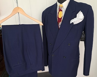 May include: A navy blue double-breasted suit jacket with a white collared shirt, a red tie with yellow and blue circular patterns, and a white pocket square. The matching navy blue trousers are displayed on a wooden hanger nearby.