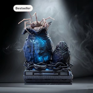 Op de afbeelding: Gedetailleerde sculptuur van een alien-ei en facehugger, met een blauw en zwart kleurenschema. De facehugger komt uit een grote, getextureerde eivormige structuur. De sculptuur staat op een grijze basis en heeft een "Bestseller" label.