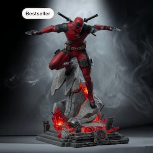 May include: A red and black Deadpool figurine in a dynamic pose, standing on a rocky base with glowing red accents. The figure has two swords on its back and is a bestseller.
