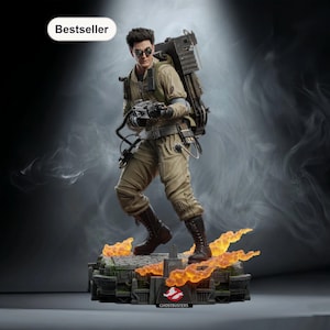 Op de afbeelding: Gedetailleerd beeldje van een Ghostbusters-personage in een beige jumpsuit, met een protonenpack en een pistool. Het beeldje staat op een voet met vlammen en het Ghostbusters-logo. Het woord "Bestseller" staat linksboven.