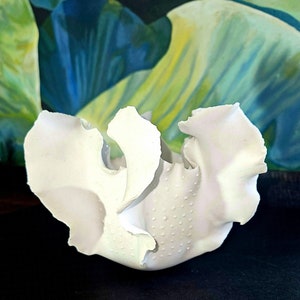 Könnte beinhalten: Weiße Keramikskulptur mit einer gerüschten, organischen Form. Die Skulptur hat eine strukturierte Oberfläche mit kleinen Punkten.