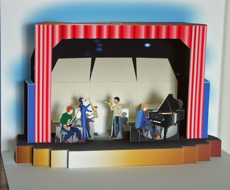 May include: A pop-up card depicting a jazz band on stage. The stage has red curtains, and the band includes a pianist, saxophonist, guitarist, and trumpeter. The background is a dark blue with white accents.